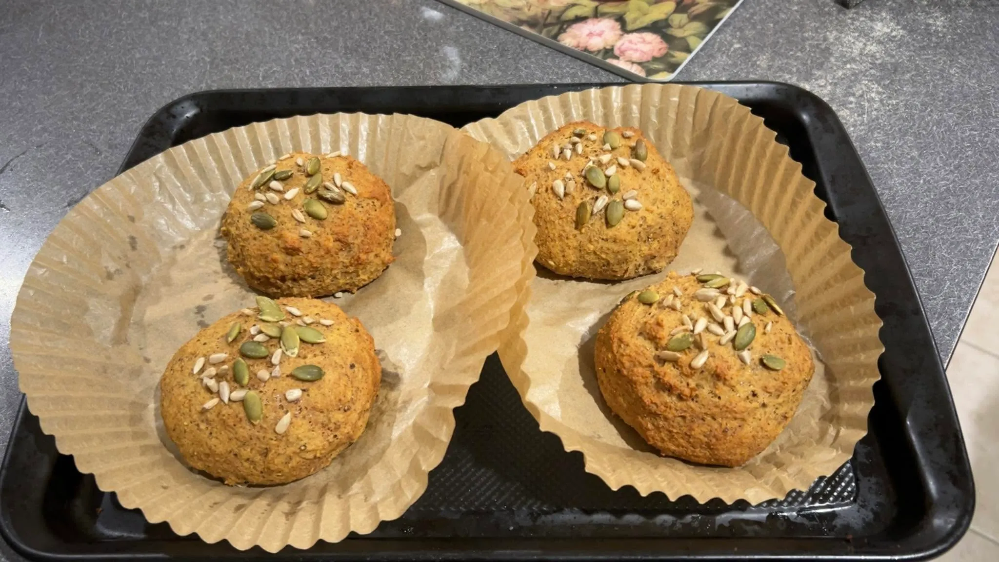 Four freshly baked seeded muffins in parchment cases on a baking tray