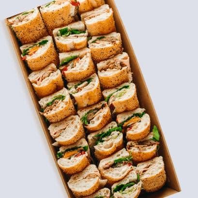Catering box packed with assorted sliced baguette sandwiches and filled rolls